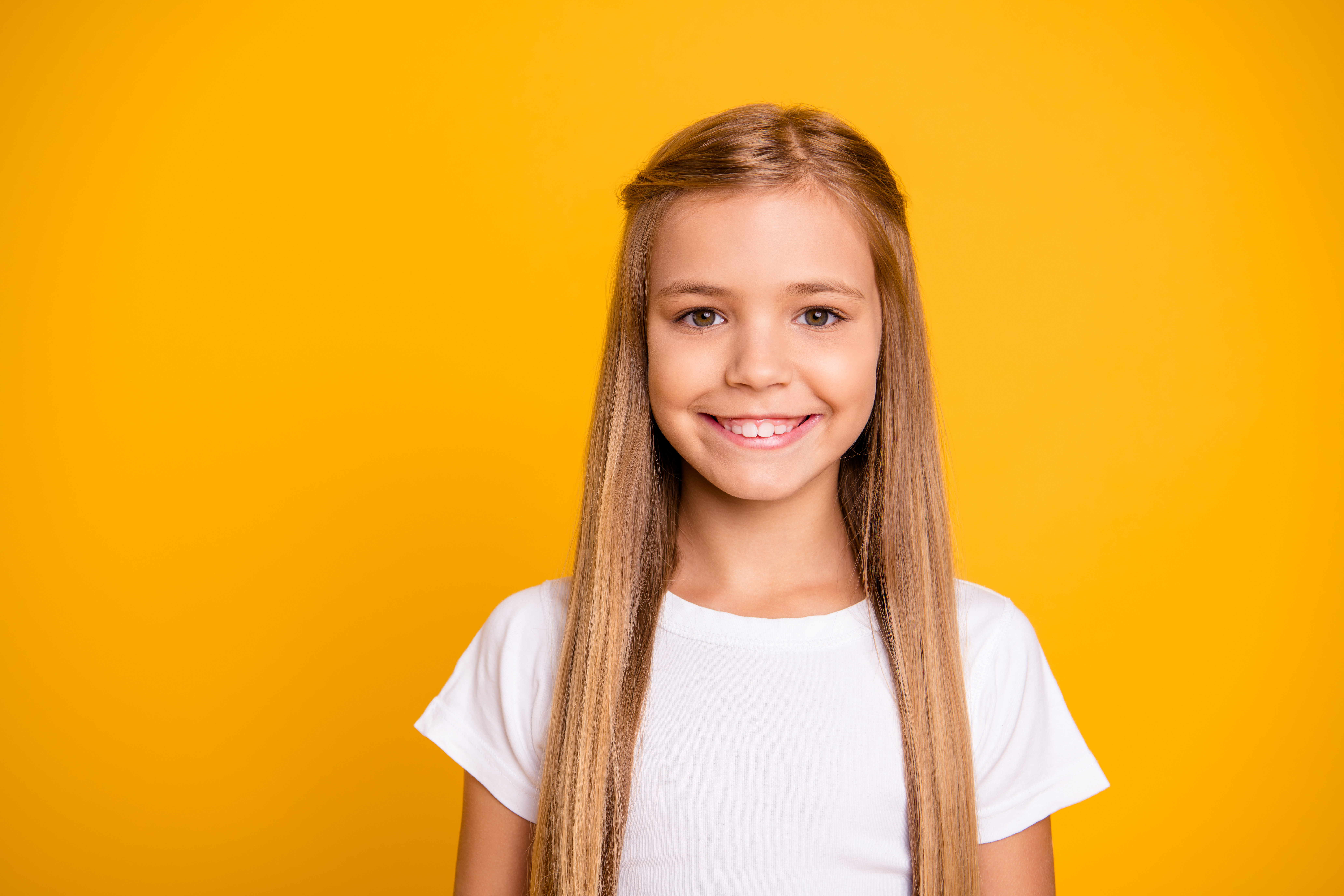 Tri-City Orthodontics - Young girl smiling in front of yellow background